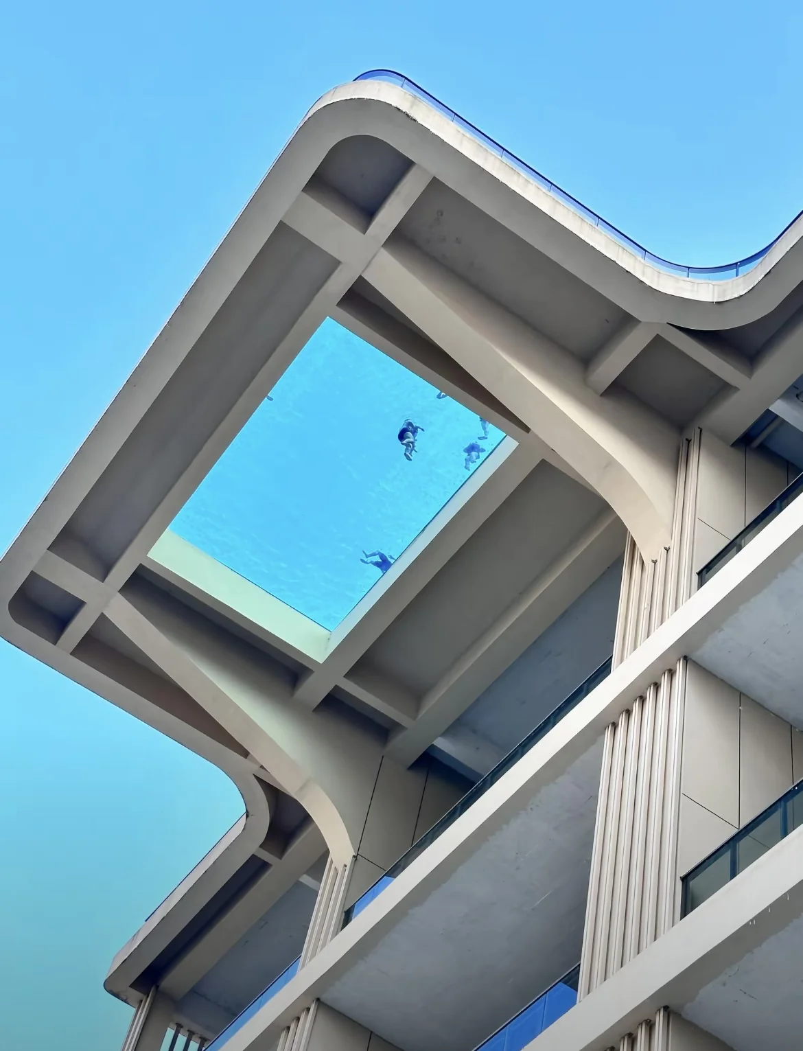 Suspended pool viewed from below, with swimmers visible through the transparent floor.